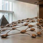 Fotografía conceptual en un lobby corporativo mostrando una escultura de una red horizontal interconectada desplazando a una pirámide vertical rígida.